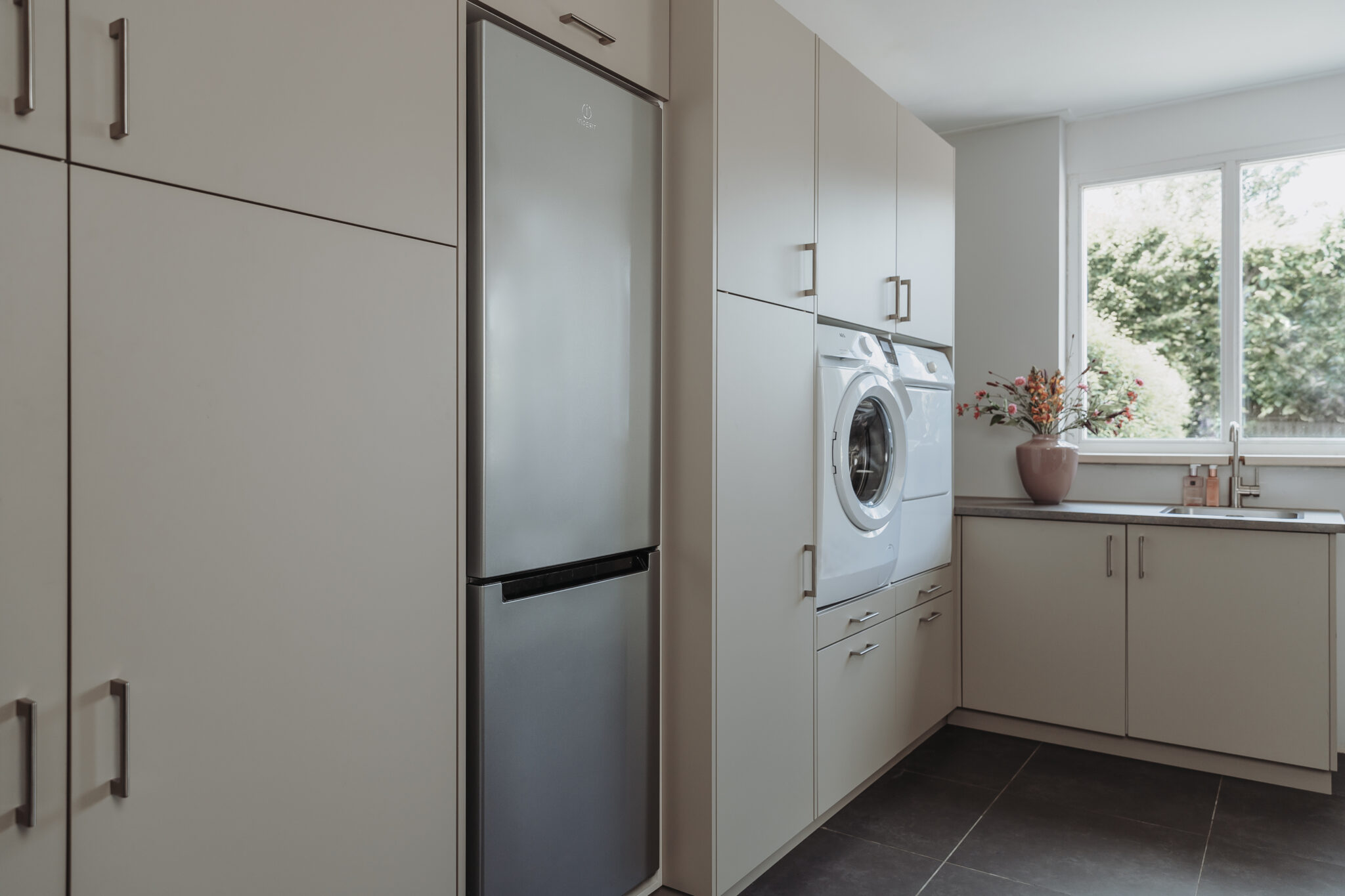Bijkeuken met ingebouwde kasten, koelkast, wasmachine en droger bij raam.