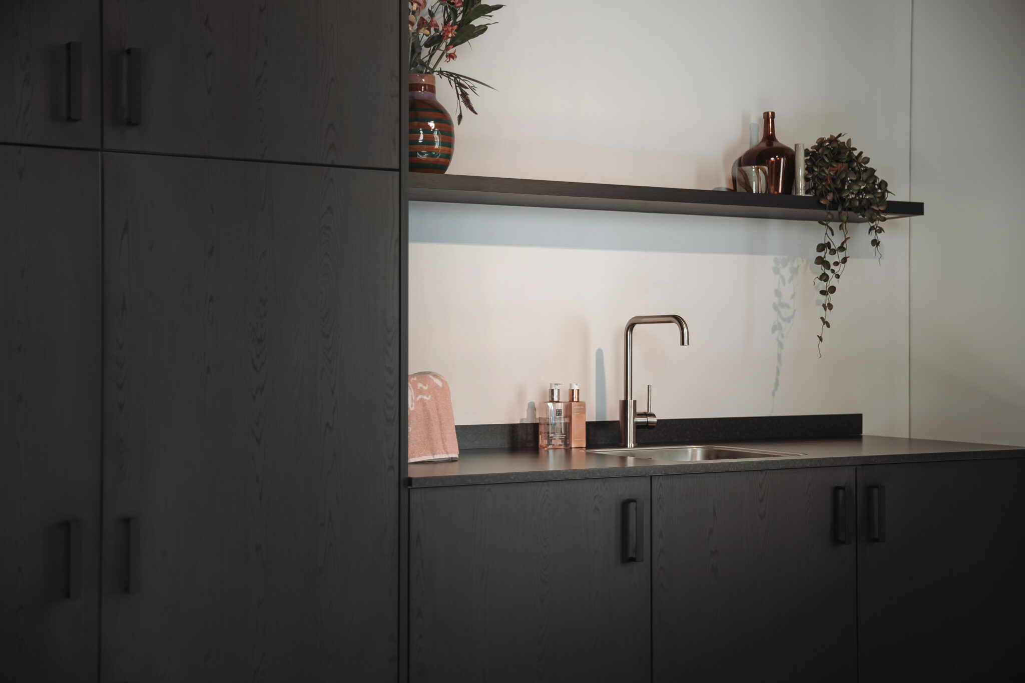 Moderne bijkeuken met donkere kasten, een wastafel en een plank met decoraties.