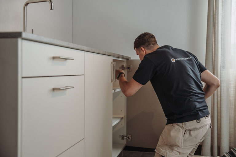 Monteur die een pantry monteert met lichtgrijze kasten en roestvrijstalen handgrepen.